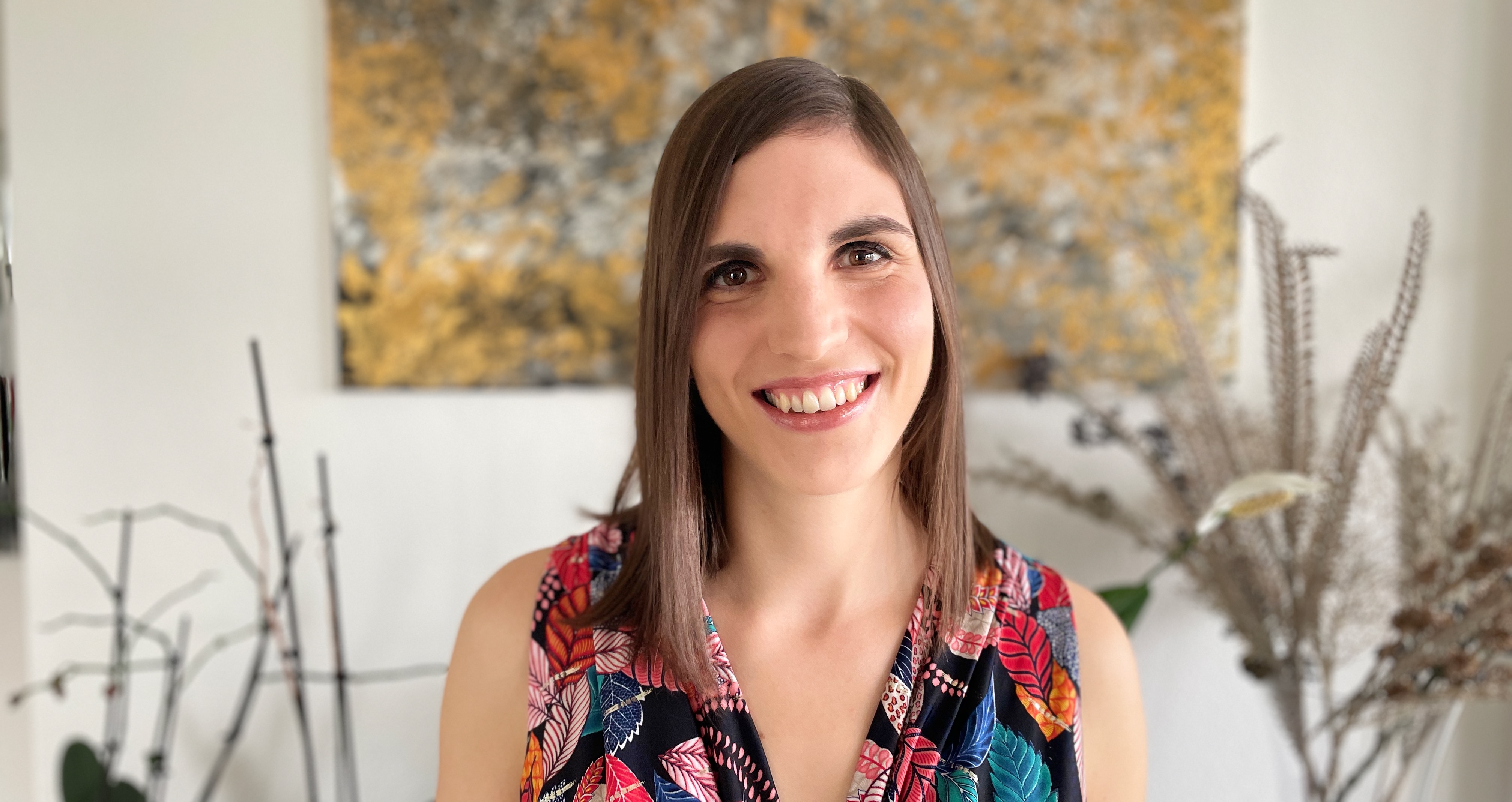 Profile photo of the author with flowers and a gold and silver painting in the background.